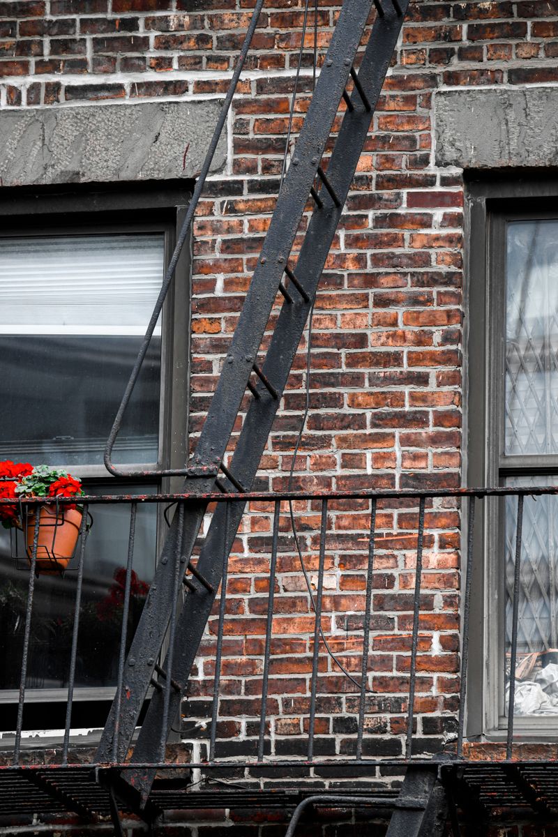 A classic red brick building in NYC featuring a fire escape and potted flowers.