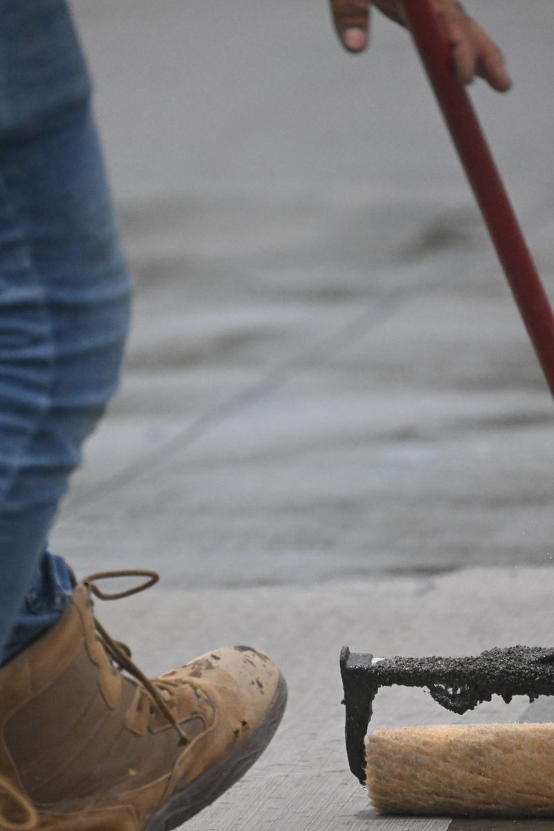 Detailed image of concrete sealing with a roller on pavement, showing boots and jeans in action.