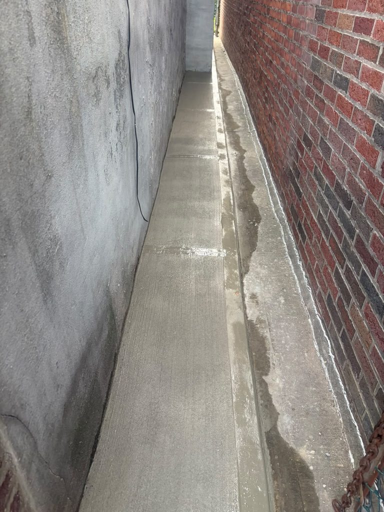  New concrete walkway pitched away from foundation wall following basement waterproofing project in Bed-Stuy.